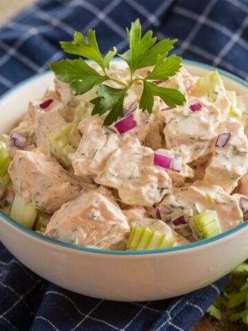 Classic Chicken Salad Chick Recipe – Creamy Chicken Salad with Tender Chicken, Crisp Celery, Red Onion, and Fresh Parsley in a White Bowl, Served on a Rustic Wooden Table with a Blue Checkered Napkin.