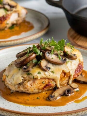 Alice Springs Chicken Recipe - A beautifully plated chicken breast topped with melted cheese, sautéed mushrooms, crispy bacon, and fresh herbs, served with a rich honey mustard sauce.