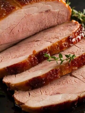 Sliced, juicy smoked pork loin with a caramelized glaze and fresh thyme garnish, highlighting a flavorful smoked pork loin recipe.