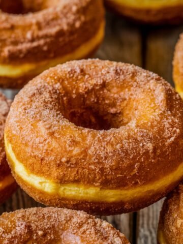 A close-up of homemade pumpkin donuts coated in a cinnamon-sugar blend, showcasing their golden-brown, fluffy texture. These deep-fried treats are bursting with warm fall flavors, making them a perfect seasonal indulgence.