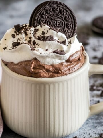 A rich and chocolatey Oreo mug cake recipe topped with fluffy whipped cream, crushed Oreo pieces, and a whole Oreo cookie, served in a ribbed ceramic mug. A quick and easy dessert made in minutes with simple ingredients.