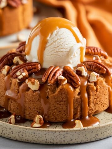 A rich and gooey Pumpkin Dump Cake Recipe topped with a scoop of vanilla ice cream, drizzled with caramel sauce, and garnished with crunchy pecans. A warm and cozy fall dessert perfect for the holiday season.