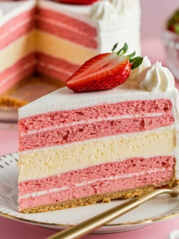 A beautifully layered Strawberry Cheesecake Cake Recipe featuring alternating layers of fluffy strawberry cake, creamy cheesecake, and velvety cream cheese frosting. Garnished with fresh strawberries and piped whipped cream, this indulgent dessert is the perfect combination of fruity and creamy flavors. A delightful treat for any occasion!