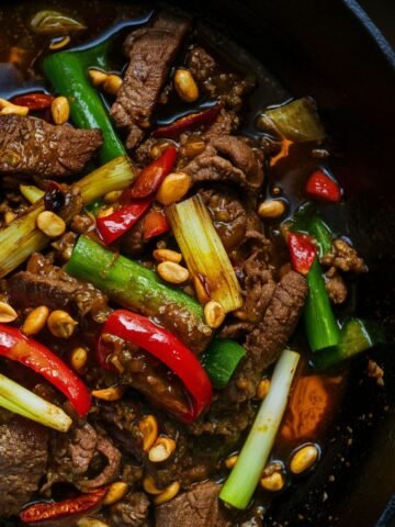 Homemade Kung Pao Beef with tender beef strips, red chilies, scallions, bell peppers, and peanuts in a glossy spicy-sweet sauce, served in a cast iron skillet.
