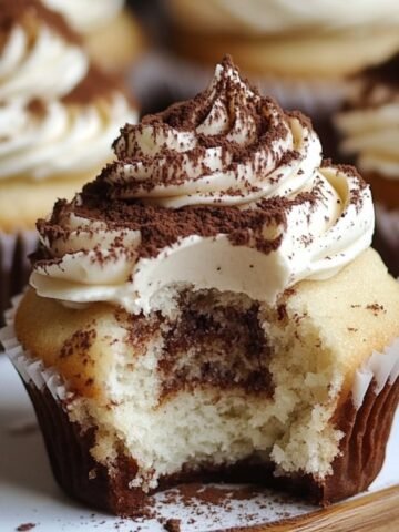 Homemade tiramisu cupcakes with mascarpone frosting and cocoa dusting, bitten to reveal a soft, coffee-soaked center.