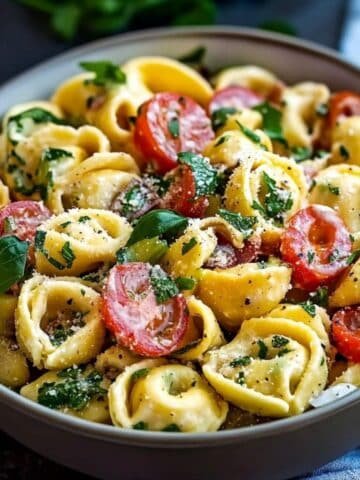 Homemade tortellini pasta salad with cheese tortellini, cherry tomatoes, fresh herbs, and grated Parmesan in a ceramic bowl.