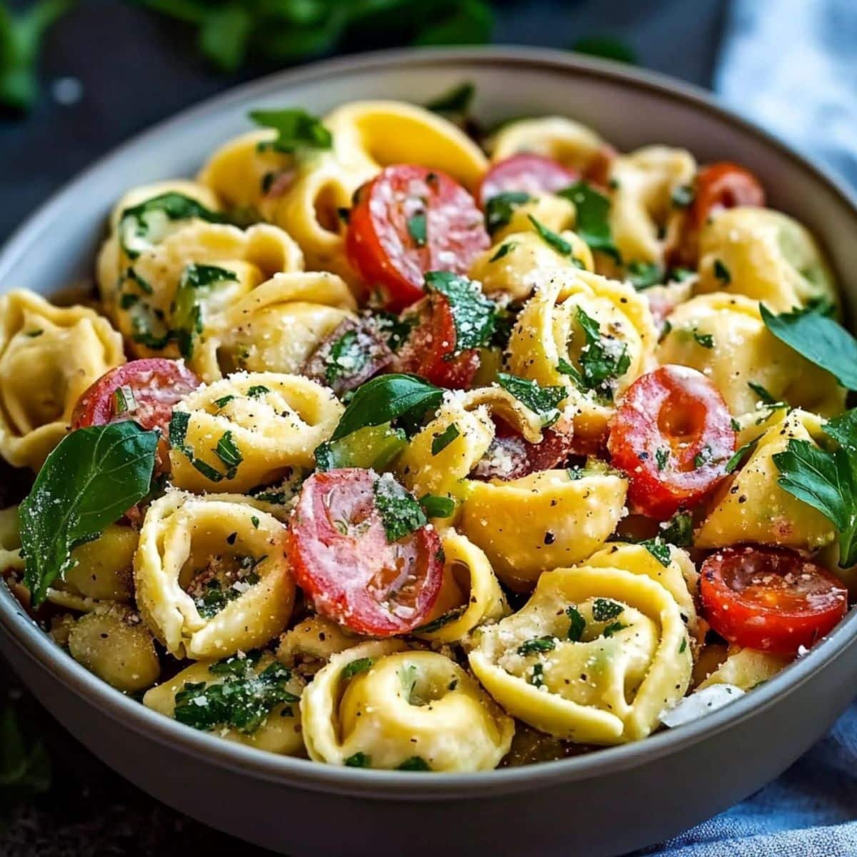 Homemade tortellini pasta salad with cheese tortellini, cherry tomatoes, fresh herbs, and grated Parmesan in a ceramic bowl.