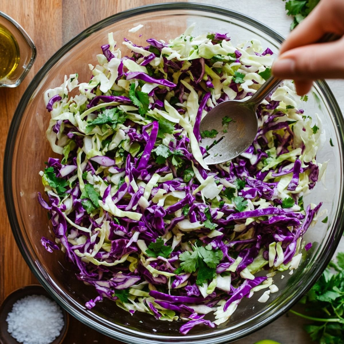Freshly mixed slaw for fish tacos with green and purple cabbage, cilantro, and lime in a glass bowl.