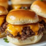 Homemade cheeseburger sliders on a white plate with melted cheddar, juicy ground beef, and golden Hawaiian rolls, garnished with parsley.