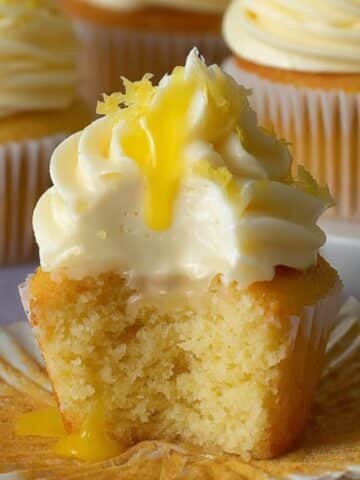 Homemade lemon cupcakes with lemon buttercream, lemon curd drizzle, and a bite showing its soft, fluffy crumb.