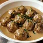 Homemade Swedish meatballs in creamy brown gravy, topped with fresh parsley, served in a white bowl.