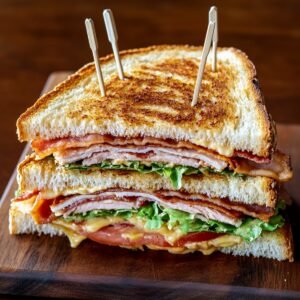 Triple-decker homemade club sandwich with turkey, bacon, lettuce, tomato, and mayo, secured with toothpicks and stacked on a wooden board.