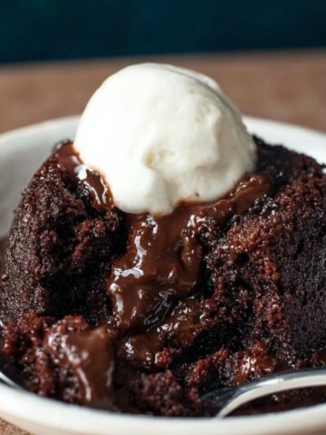 Homemade chocolate pudding cake with a gooey molten center, topped with a scoop of vanilla ice cream in a white bowl.