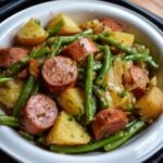 Homemade Kielbasa Green Beans and Potatoes, baby potatoes, and green beans, tossed with onions and herbs, served in a white dish with a black rim.