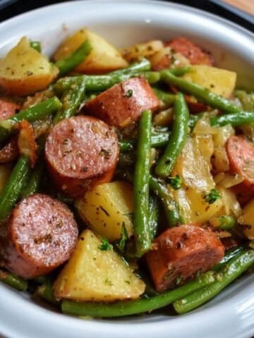 Homemade Kielbasa Green Beans and Potatoes, baby potatoes, and green beans, tossed with onions and herbs, served in a white dish with a black rim.