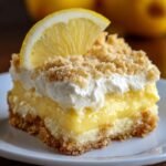 Homemade lemon cream cheese dump cake with layers of creamy filling, lemon pudding, whipped topping, and a crumbly crust, topped with a lemon slice.