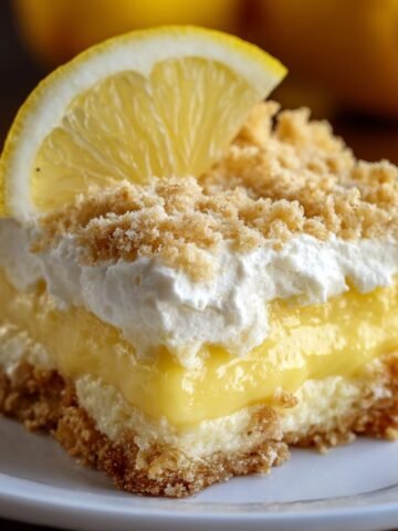 Homemade lemon cream cheese dump cake with layers of creamy filling, lemon pudding, whipped topping, and a crumbly crust, topped with a lemon slice.