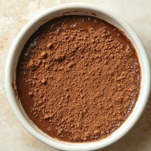 Unbaked chocolate pudding cake topped with a thick layer of dry cocoa powder in a white ramekin.