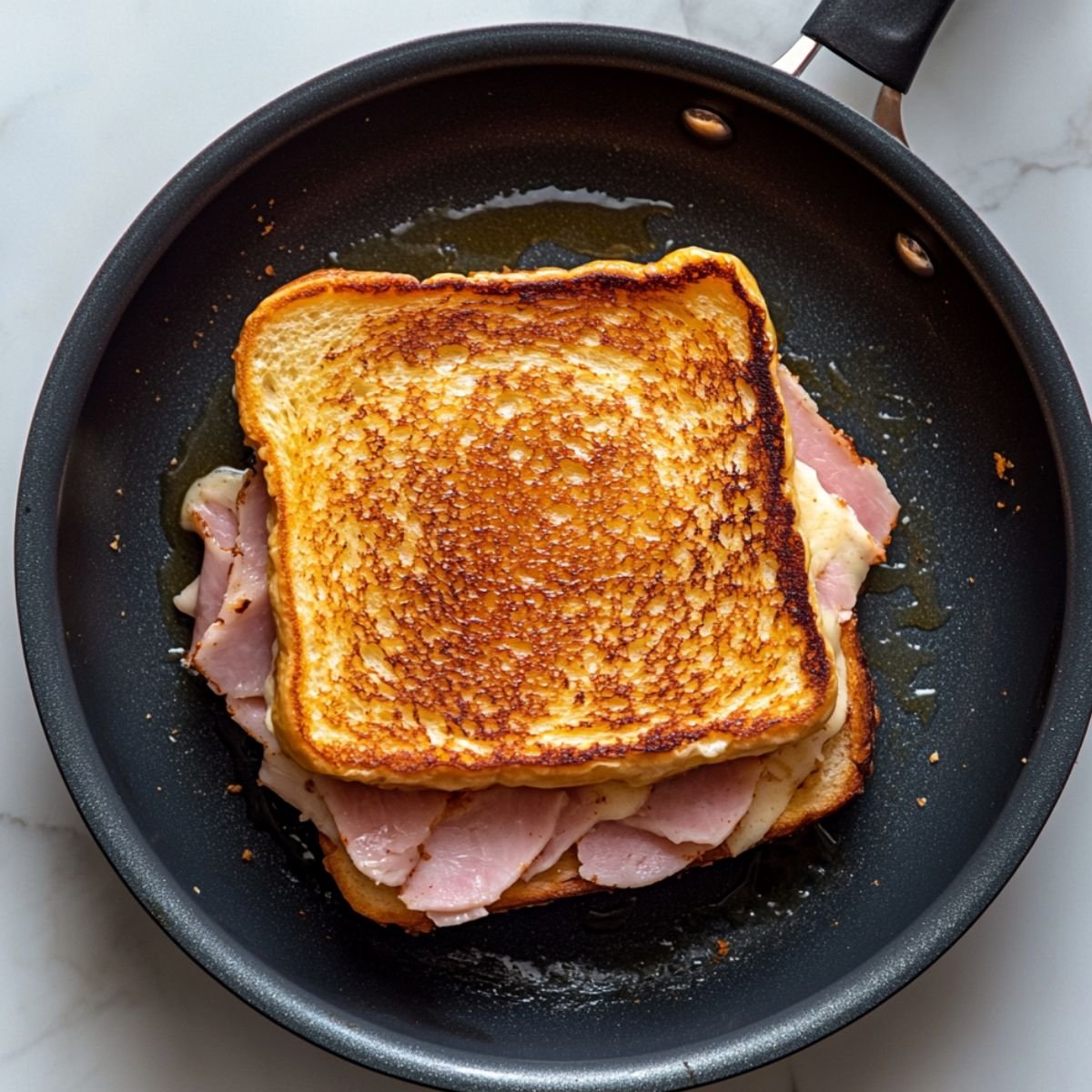 A golden-brown Monte Cristo sandwich with ham and cheese cooking in a nonstick skillet, crisped to perfection and sizzling in melted butter.
