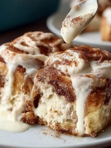 Best Tres Leches Cinnamon Rolls topped with whipped cream and cinnamon, served with a fork on a white plate.