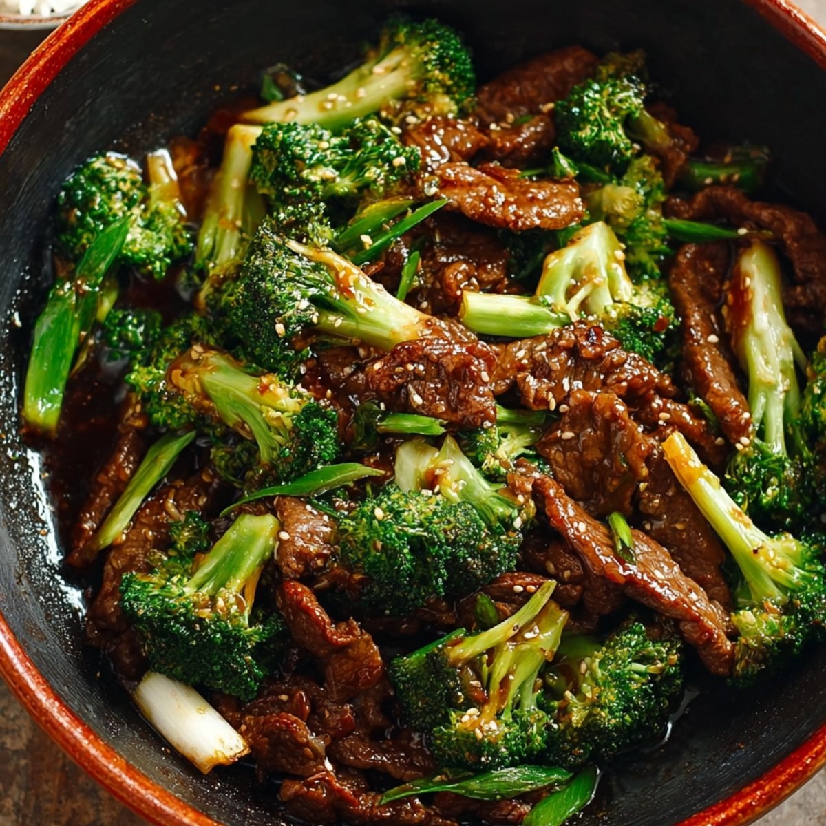 Homemade Chinese Beef and Broccoli over steamed white rice in a ceramic bowl, tender beef in glossy brown sauce with vibrant broccoli, natural daylight.