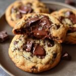 Homemade Chocolate Chip Cookies with large melted chocolate chunks, one broken open to reveal a gooey chocolate center, on a dark plate.