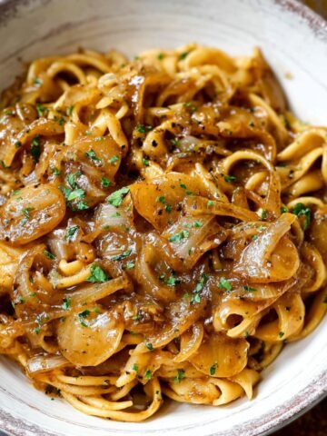 Homemade French Onion Pasta coated in caramelized onion sauce, topped with parsley, served in a rustic ceramic bowl with a fork.