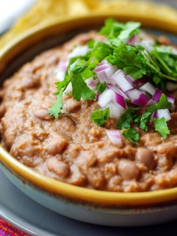 Homemade refried beans in a bowl topped with fresh cilantro and red onion