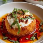The Best Fried Burrata Recipe in a beige bowl with chili oil, sun-dried tomatoes, basil leaves, and microgreens on top.