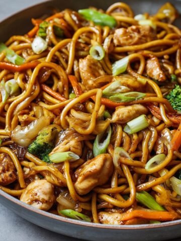 Chicken Lo Mein Recipe in a skillet with glossy noodles, tender chicken pieces, broccoli florets, carrots, onions, and scallions tossed in a rich soy-based sauce — perfectly caramelized and ready to serve, showing real home-cooked texture and freshness.