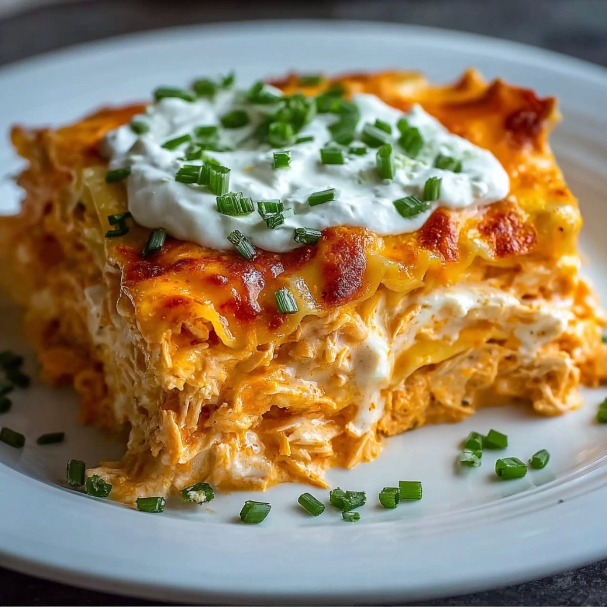Easy Buffalo Chicken Lasagna slice on a white plate, showing layers of creamy shredded chicken in orange buffalo sauce, melted cheese, and golden-browned top, sprinkled with fresh parsley.