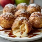 Homemade Apple Pie Bombs on a white plate, golden and sugar-dusted, one cut open showing warm caramel apple filling and cream sauce, cozy homemade feel with warm light.