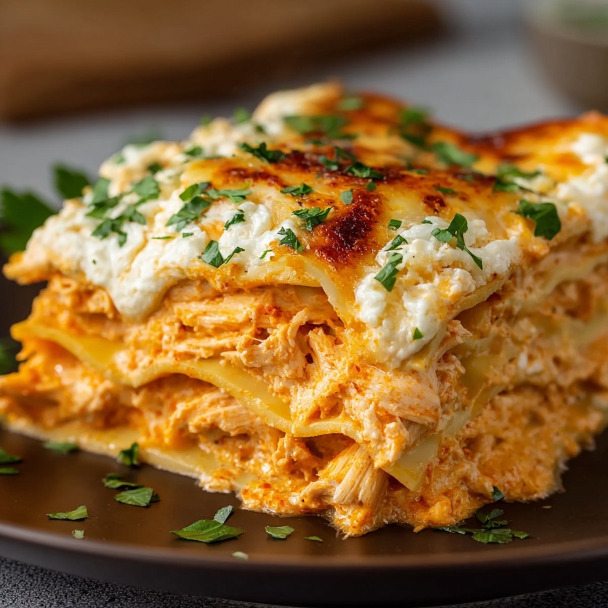 Homemade Buffalo chicken lasagna slice topped with creamy ranch and fresh chopped chives, showing layers of shredded chicken, melted cheese, and noodles on a white plate.