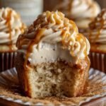 Homemade Harry Potter butterbeer cupcakes with creamy caramel-drizzled frosting, one bitten to show soft, fluffy inside, resting on a book with more cupcakes blurred in the background under warm, cozy lighting.