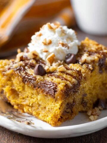 Homemade Pumpkin Earthquake Cake with whipped cream, chocolate chips, pecans, and caramel drizzle on a white plate.