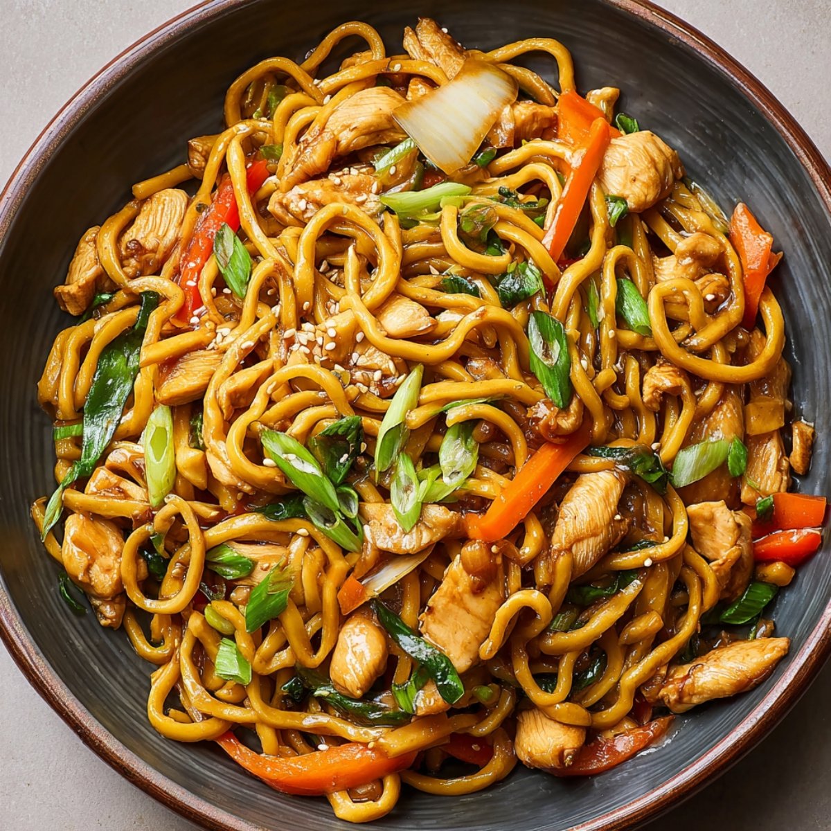 Homemade chicken lo mein recipe in a skillet with glossy noodles, tender chicken pieces, broccoli florets, carrots, onions, and scallions tossed in a rich soy-based sauce — perfectly caramelized and ready to serve, showing real home-cooked texture and freshness.