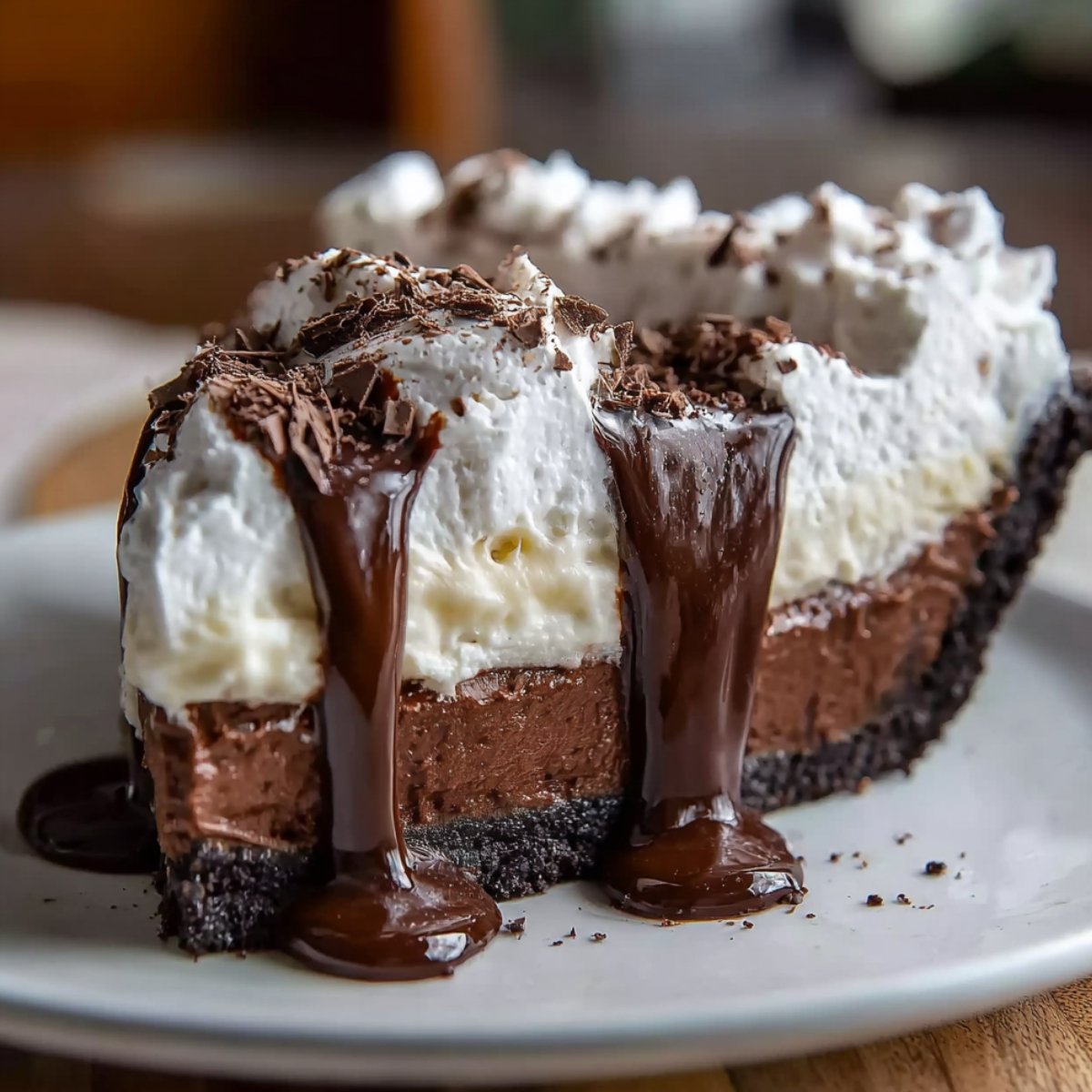 Homemade Mississippi Mud Pie slice with a chocolate cookie crust, fudgy chocolate base, creamy vanilla pudding, and whipped cream topping, drizzled with thick chocolate sauce and sprinkled with crushed chocolate on a white plate.