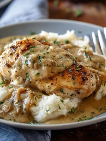 Homemade slow cooker chicken and gravy over mashed potatoes on a gray plate, topped with onion gravy and thyme, warm natural light.