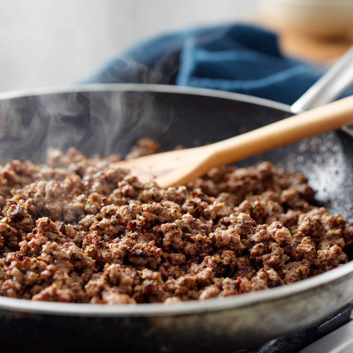 Ground beef browning in a skillet with steam rising and a wooden spatula stirring, showing a homemade, freshly cooked texture.