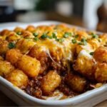 Chili Cheese Tater Tot Casserole in a white baking dish, topped with melted cheddar cheese, crispy golden tater tots, and fresh chopped green onions.