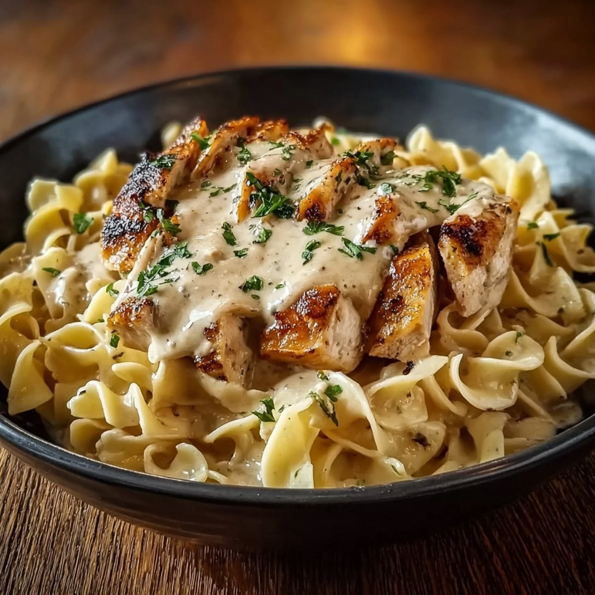 Easy Chicken with Buttered Noodles Recipe topped with creamy sauce and fresh parsley in a gray bowl.
