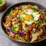 Homemade Egg Roll in a Bowl Recipe filled with ground pork, sautéed cabbage, carrots, and purple cabbage, topped with a crispy-edged sunny-side-up egg and fresh green onions.
