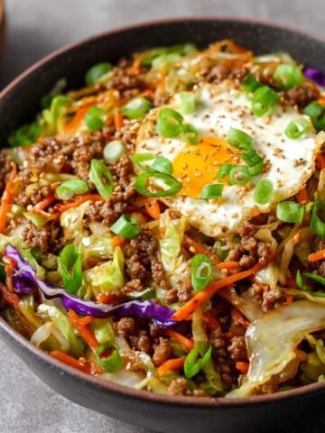 Homemade Egg Roll in a Bowl Recipe filled with ground pork, sautéed cabbage, carrots, and purple cabbage, topped with a crispy-edged sunny-side-up egg and fresh green onions.