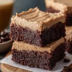Homemade Frosted Coffee Brownies stacked on parchment paper, showing a dense, fudgy chocolate base and thick, creamy coffee buttercream frosting on top, with soft texture and natural crumbs visible, set on a wooden board for a cozy, real kitchen look.