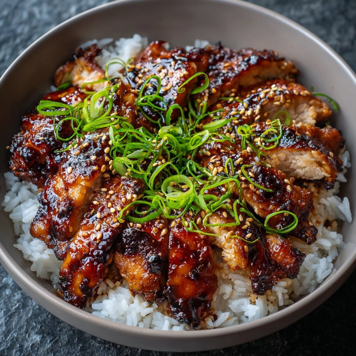 Homemade teriyaki chicken sliced over steamed white rice, glazed in a thick soy-honey sauce, and topped with toasted sesame seeds and fresh green onions.