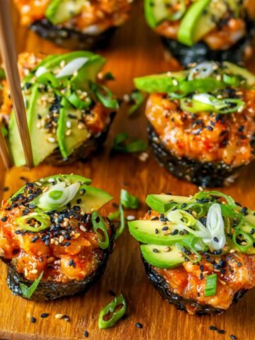 Baked Salmon Sushi Cups Recipe topped with avocado, green onions, sesame seeds, and spicy sauce, served on a plate with chopsticks.