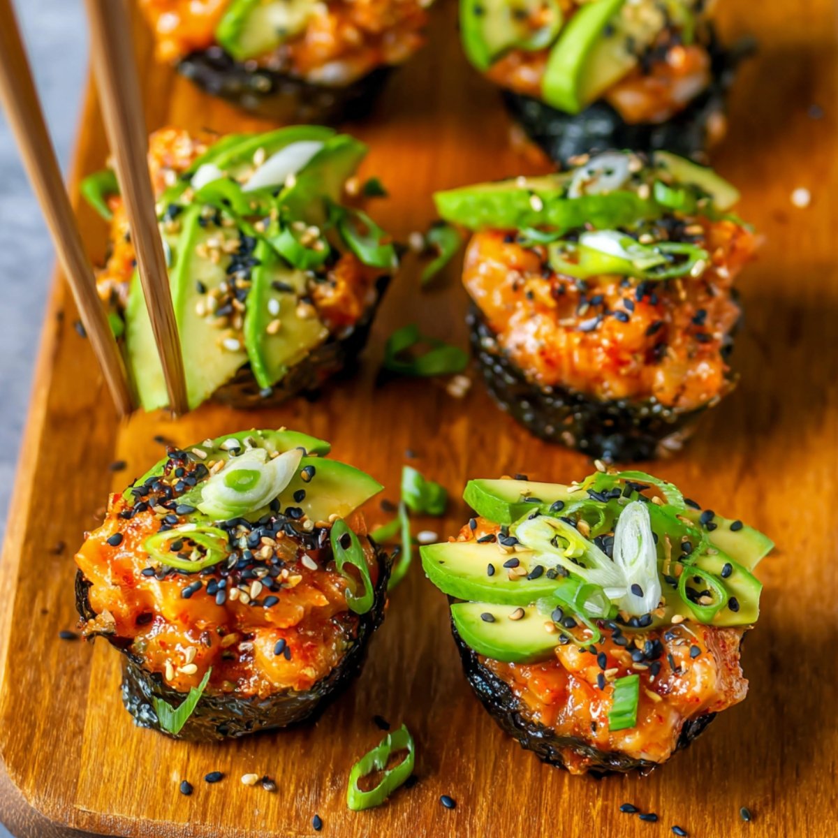 Baked Salmon Sushi Cups Recipe topped with avocado, green onions, sesame seeds, and spicy sauce, served on a plate with chopsticks.
