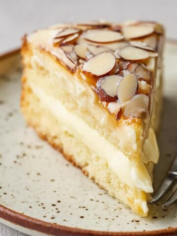 Slice of bee sting cake with creamy vanilla filling and honey-glazed almond topping on a plate.