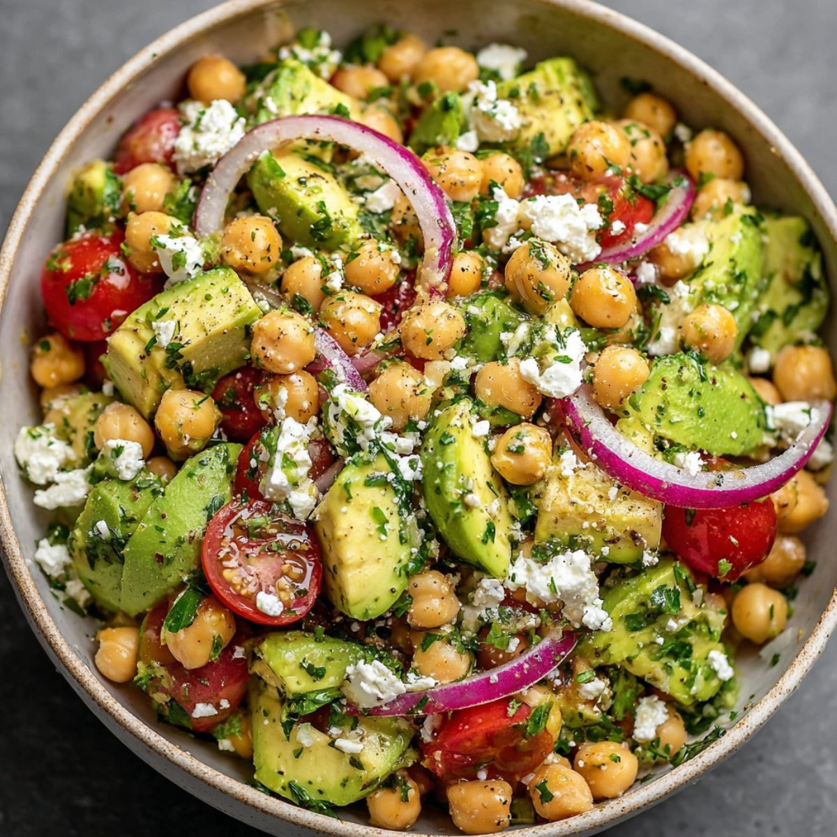 A homemade bowl of chickpea, feta, and avocado salad with cherry tomatoes, red onion, fresh herbs, and lemon vinaigrette.