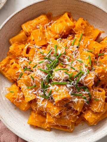 Gochujang Pasta in a creamy orange sauce, topped with grated cheese and fresh green chives, served in a bowl.